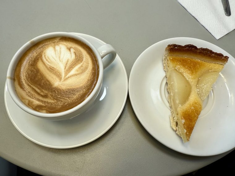 Cappuccino with rosetta latte art beside a custard pear tart