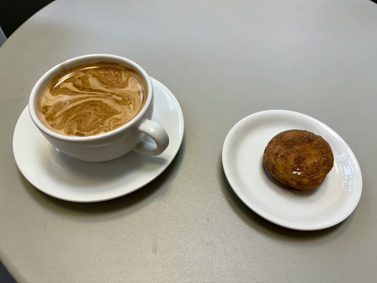 Flat white with swirled latte art and a sugared bun