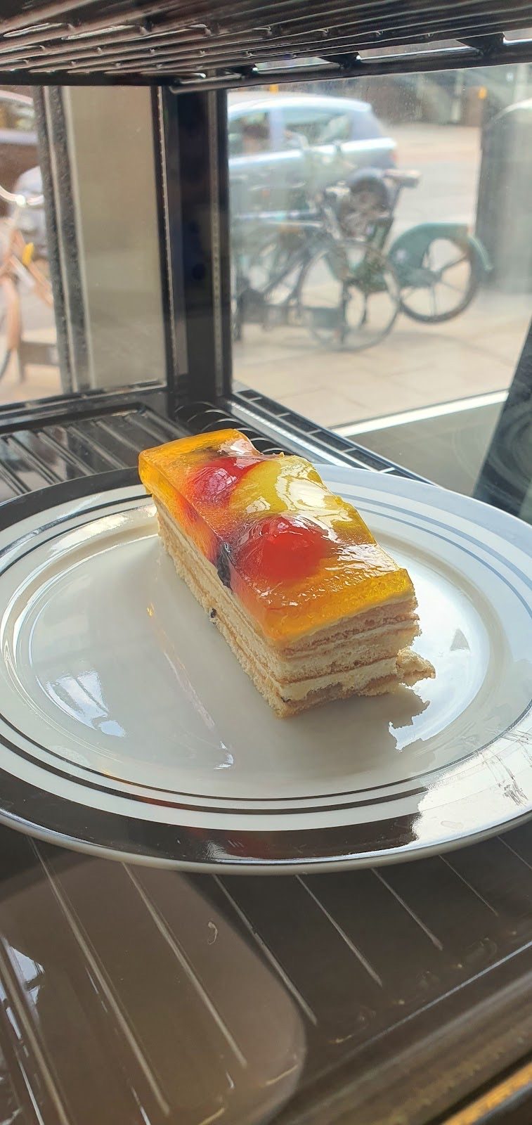 A fruit-topped mille-feuille slice on a glass stand in the display cabinet